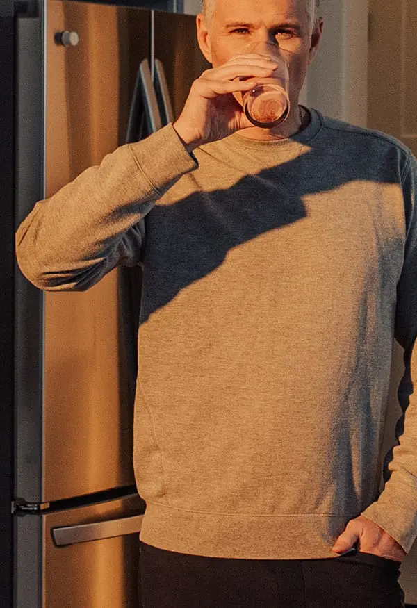 Man drinking while standing next to the fridge