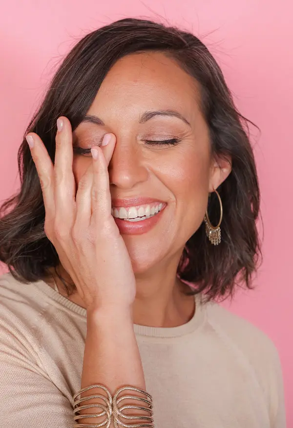 Woman smiling with hand on face against a pink background